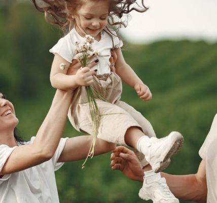 Happy family enjoying playful outdoor moment, lifting child in summer day.