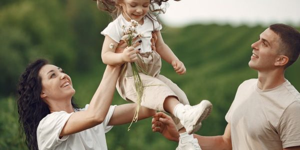 Happy family enjoying playful outdoor moment, lifting child in summer day.